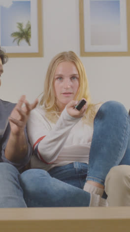 Vertical-Video-Of-Woman-Telling-Male-Friends-To-Be-Quiet-As-They-Sit-On-Sofa-At-Home-Together-To-Watch-TV